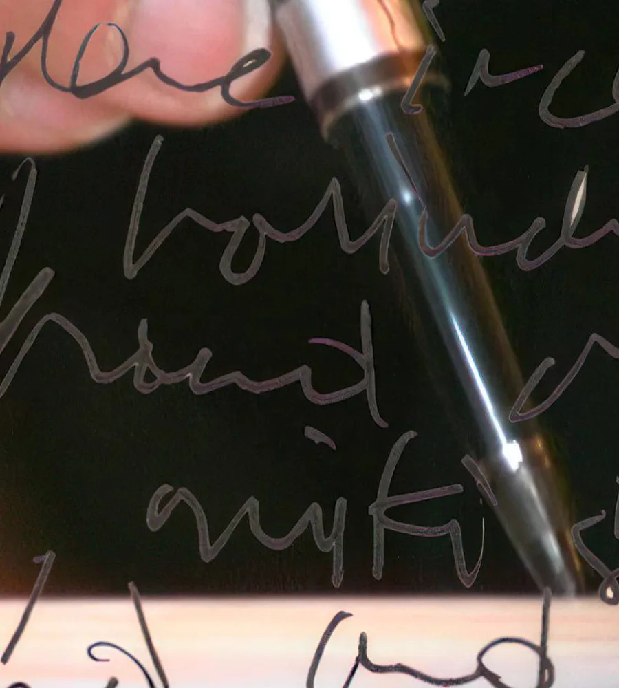 A still from Alan at Work. a hand scrawls lines of text with an ink pen