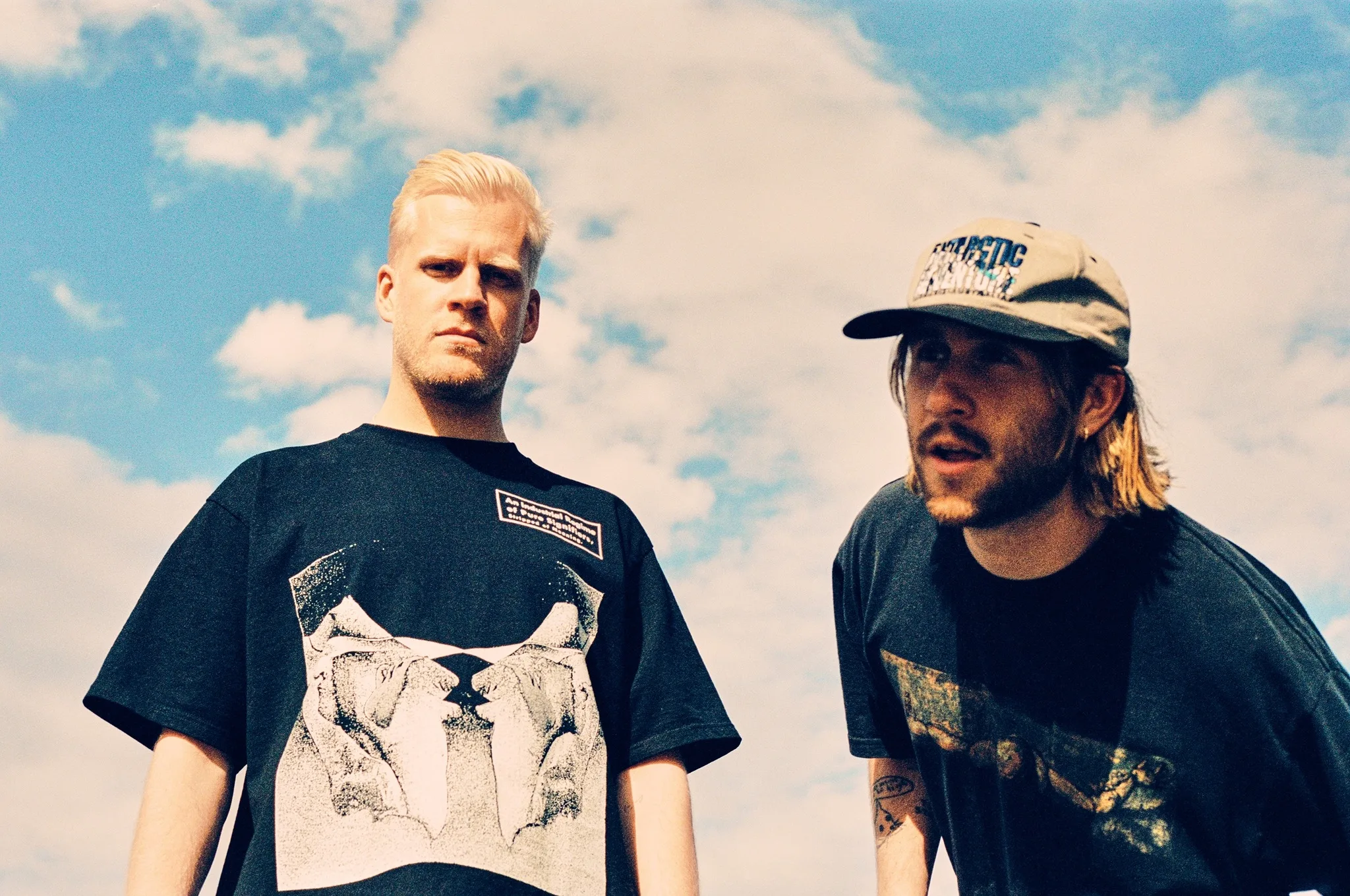 Oliver Lee and James Carter, musicians of Snakehips pose against a cloudy, blue sky.