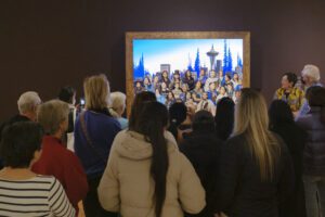 A crowd gathers in front of a painting in the American Art: The Stories We Carry exhibit
