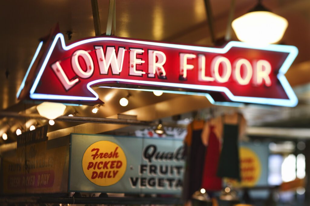 A neon sign directs to Pike Place Market's lower level at night time