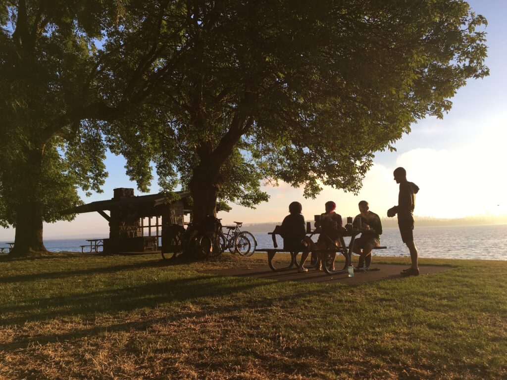 A group of cyclists drink coffee in a park as the sun rises