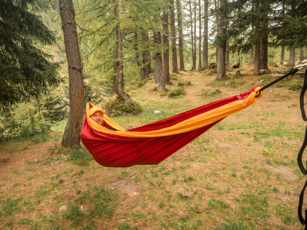 Man lies on red hammock at sunset, forest in distance