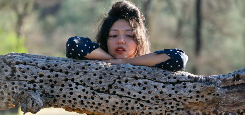 Shana Cleveland leans on a gnarled tree branch with crossed arms