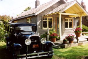 A classic car sits outside a cottage with cute landscaping in Cannon Beach, Oregon on a sunny day