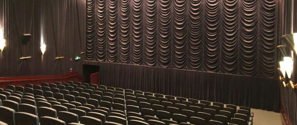 A large mocha colored curtain is down on a lit-up movie theater with empty seats at Majestic Bay Theatre in Ballard, Seattle, Washington.