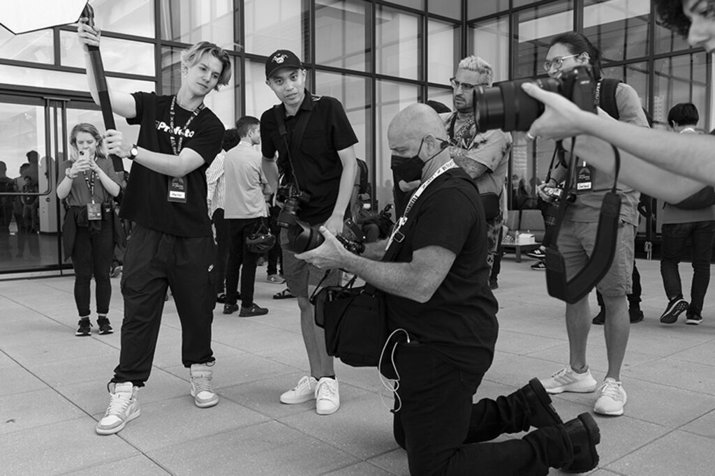 A group of photographers gather around an instructor during a workshop. The photo is in black and white