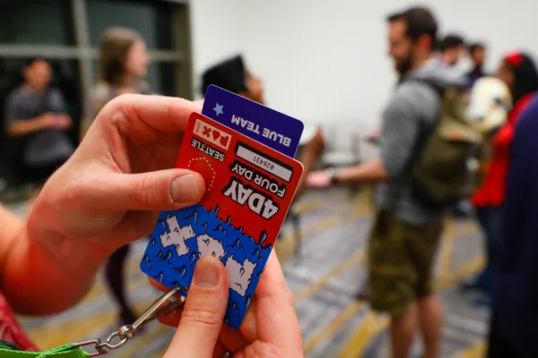 A person holds up a 4-day PAX West badge. It's orange and upside down.