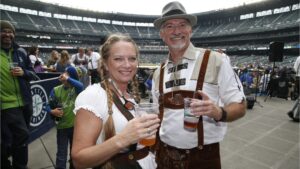 A couple poses in Oktoberfest outfits with beer at T-Mobile Park for a Mariners game.