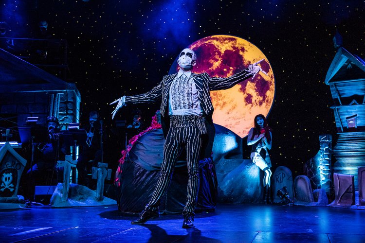 This Is Halloween promotional image showing a man painted like a skeleton dancing in front of a crimson moon stage set.