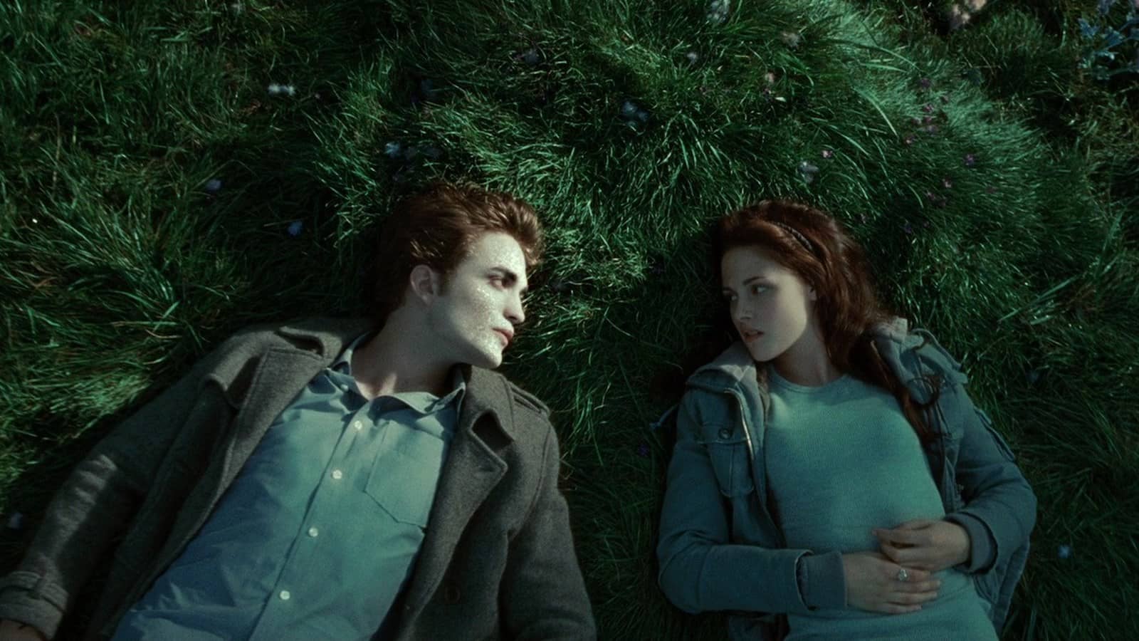 Two vampiric looking teens stare longingly at each other on blue-green grass.