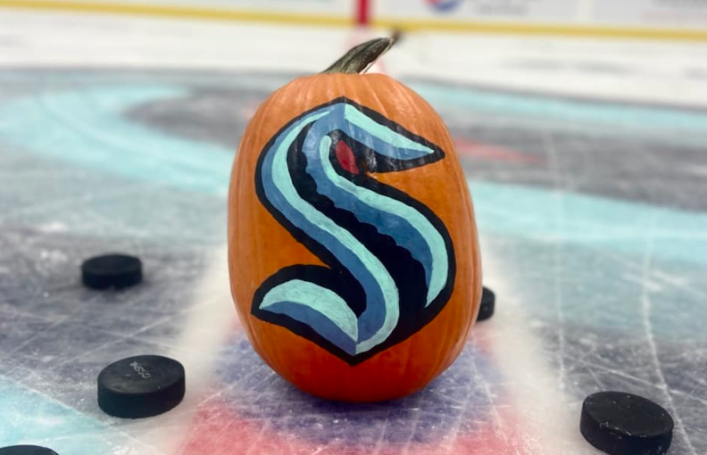 A pumpkin with the Kraken "S" logo sits in the Krakem Community Iceplex with pucks around it.