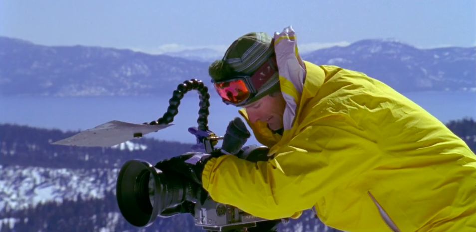 A filmmaker in a ski outfit films on camera.