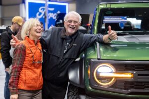 Two people lean against a new car at the 2022 Seattle International Auto Show.