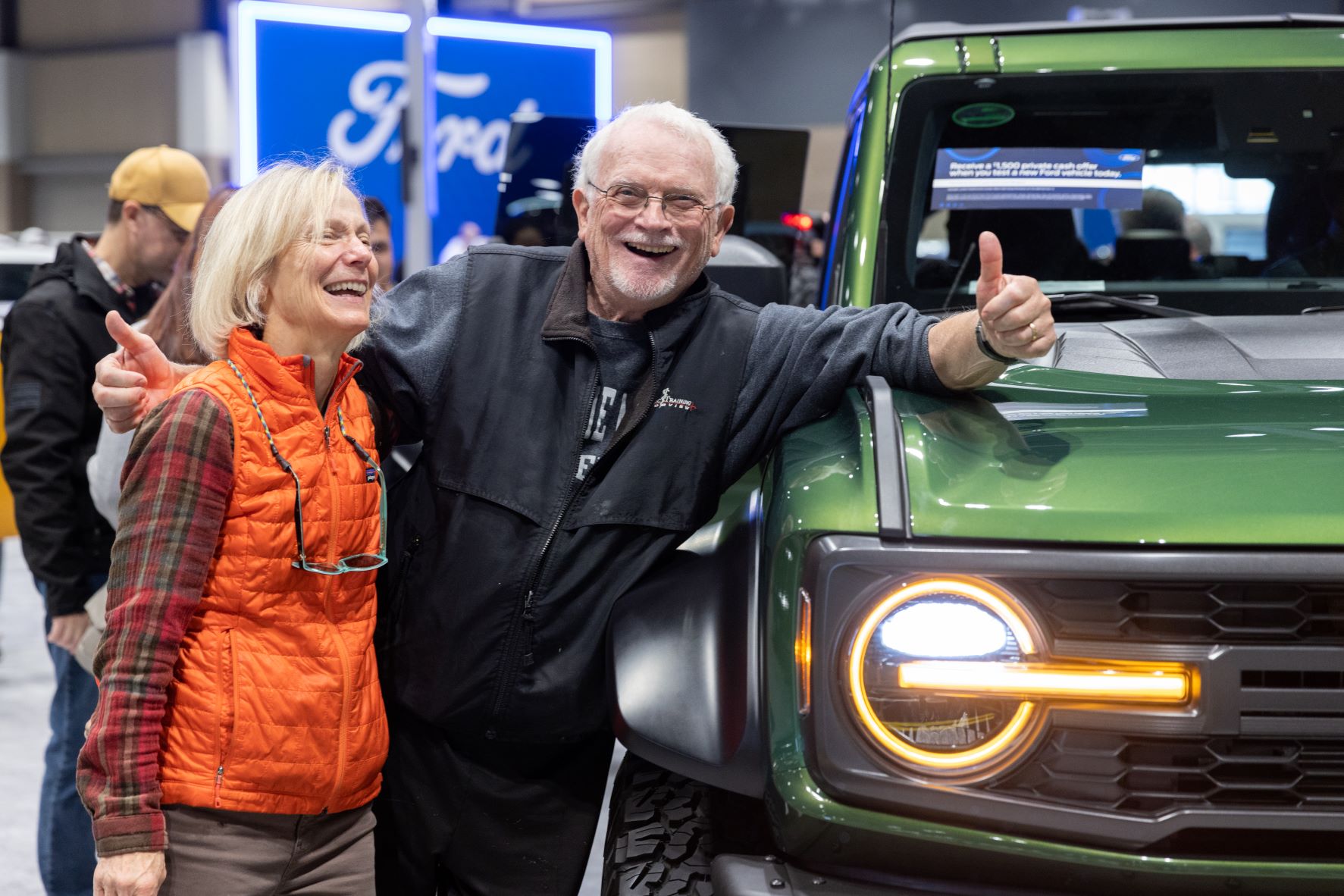 Two people lean against a new car at the 2022 Seattle International Auto Show.