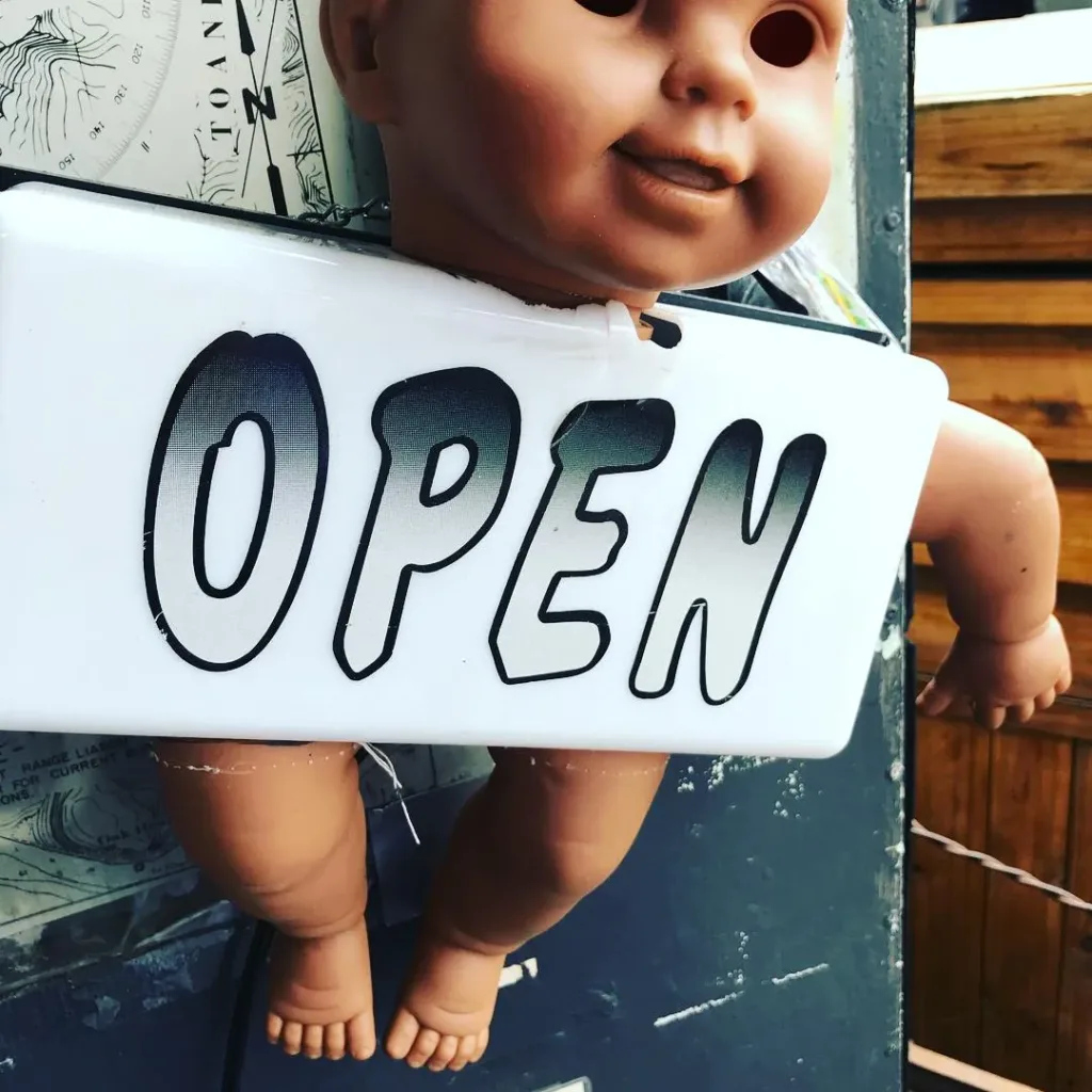 An open for business sign held up by a baby doll.