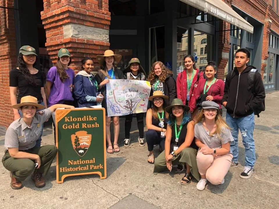 A group of people outside the National Gold Rush Museum, smiling next to sign for the museum.