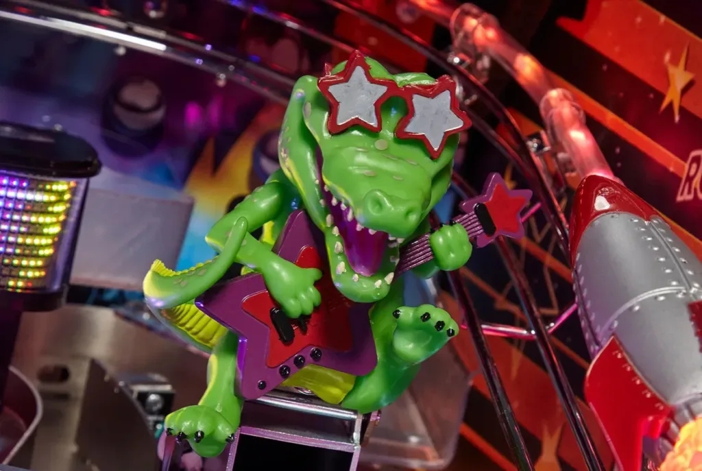 A rubber gator with Elton John-style glasses sits inside of a pinball machine.