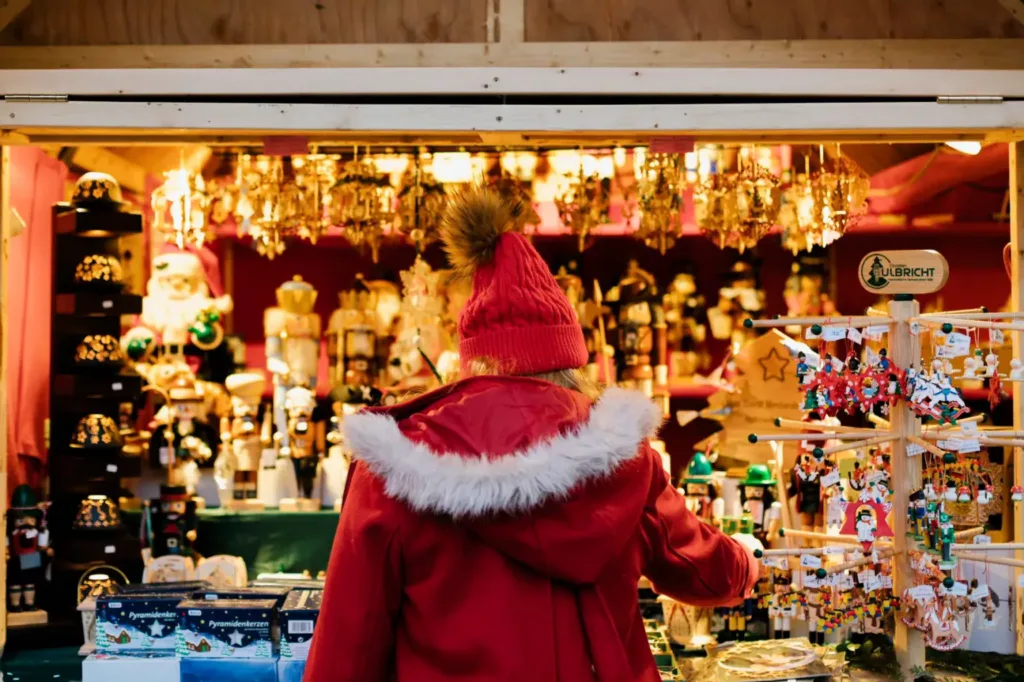 A person dressed in warm red clothing looks at Christmas gifts and ornaments at a traditional Christmas Market.