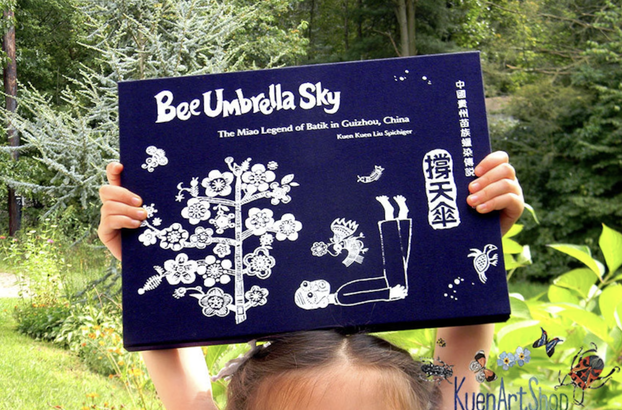 A girl holding up a copy of the book Bee Umbrella Sky