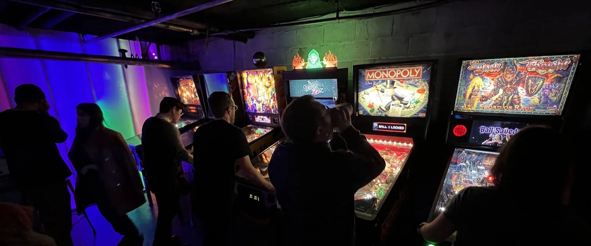 A group of people play pinball in a dark bark. Time Warp in Capitol Hill 2023 Seattle