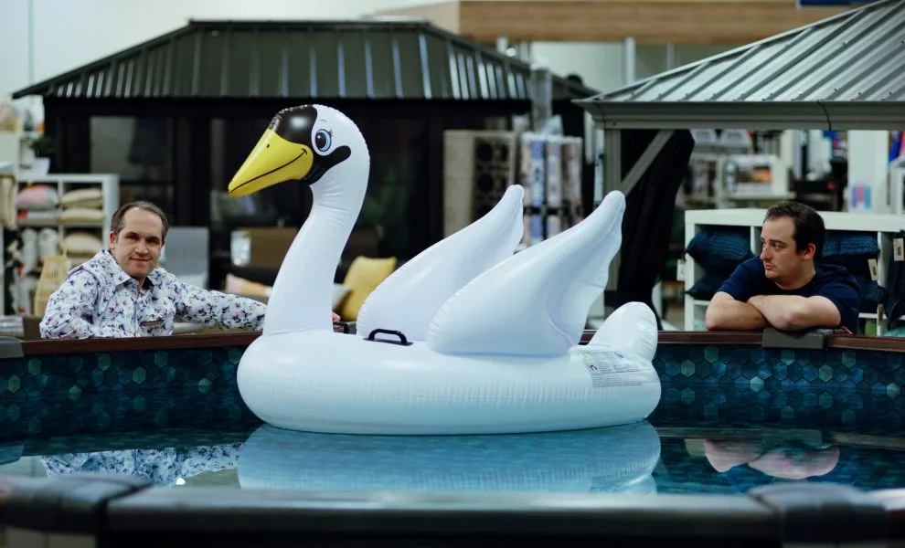 Two people look at a giant inflatable swan in a pool