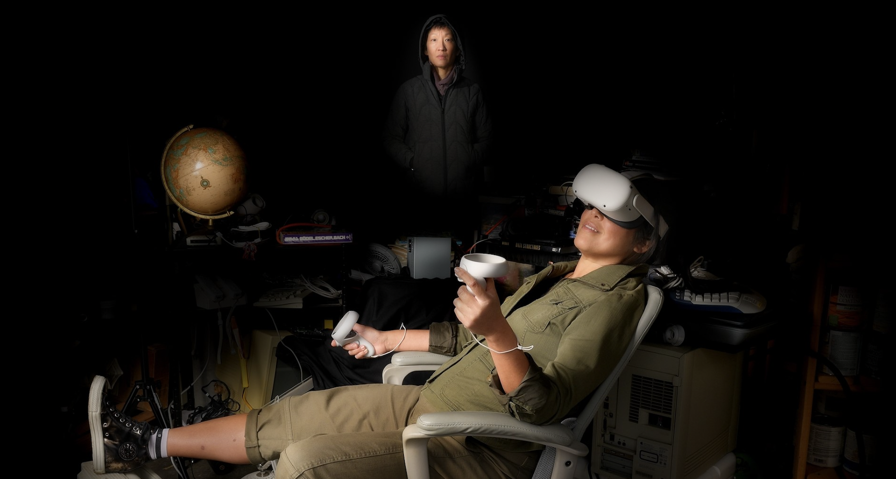 A promotional image for an upcoming show at Seattle Public Theatre featuring a person playing VR and another person in the background hovering as if they are a ghost.