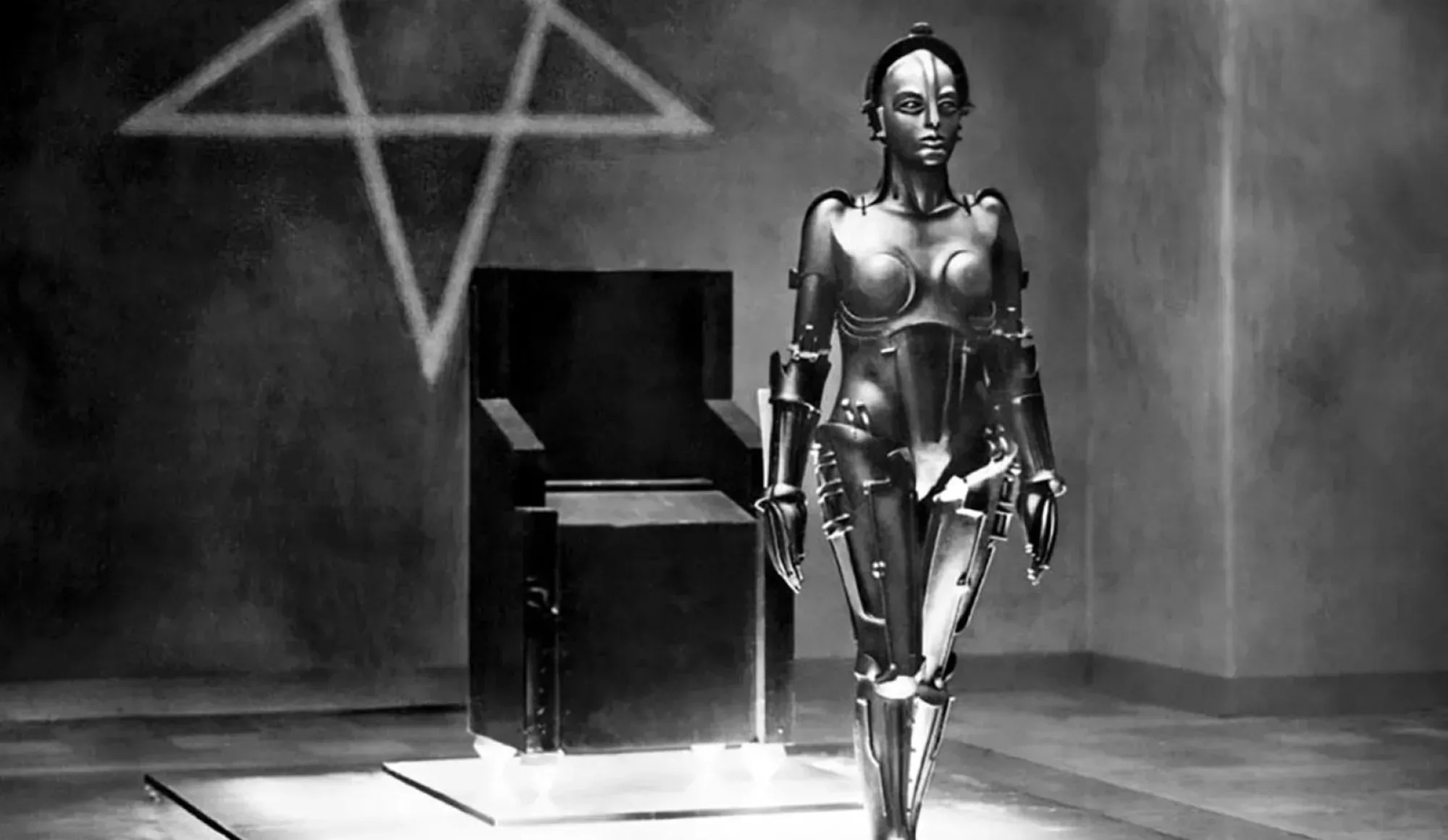 A still shot from the film Metropolis. The robot created by the evil scientist, Rotwang stands in front of a black modular chair on a platform