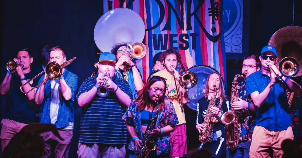A group of performers at HONK! Fest West play instruments in front of colorful sets.