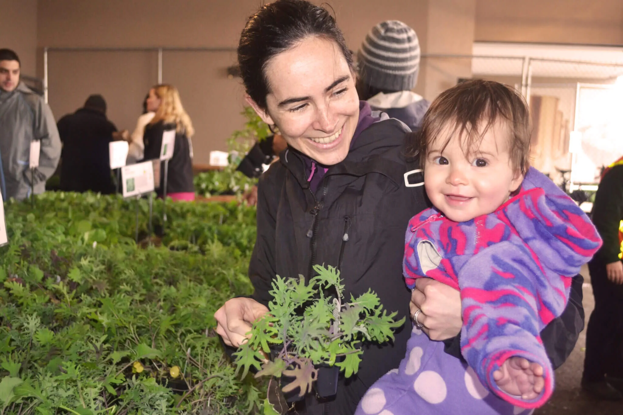 A woman looks at a smiling baby at a plant sale.