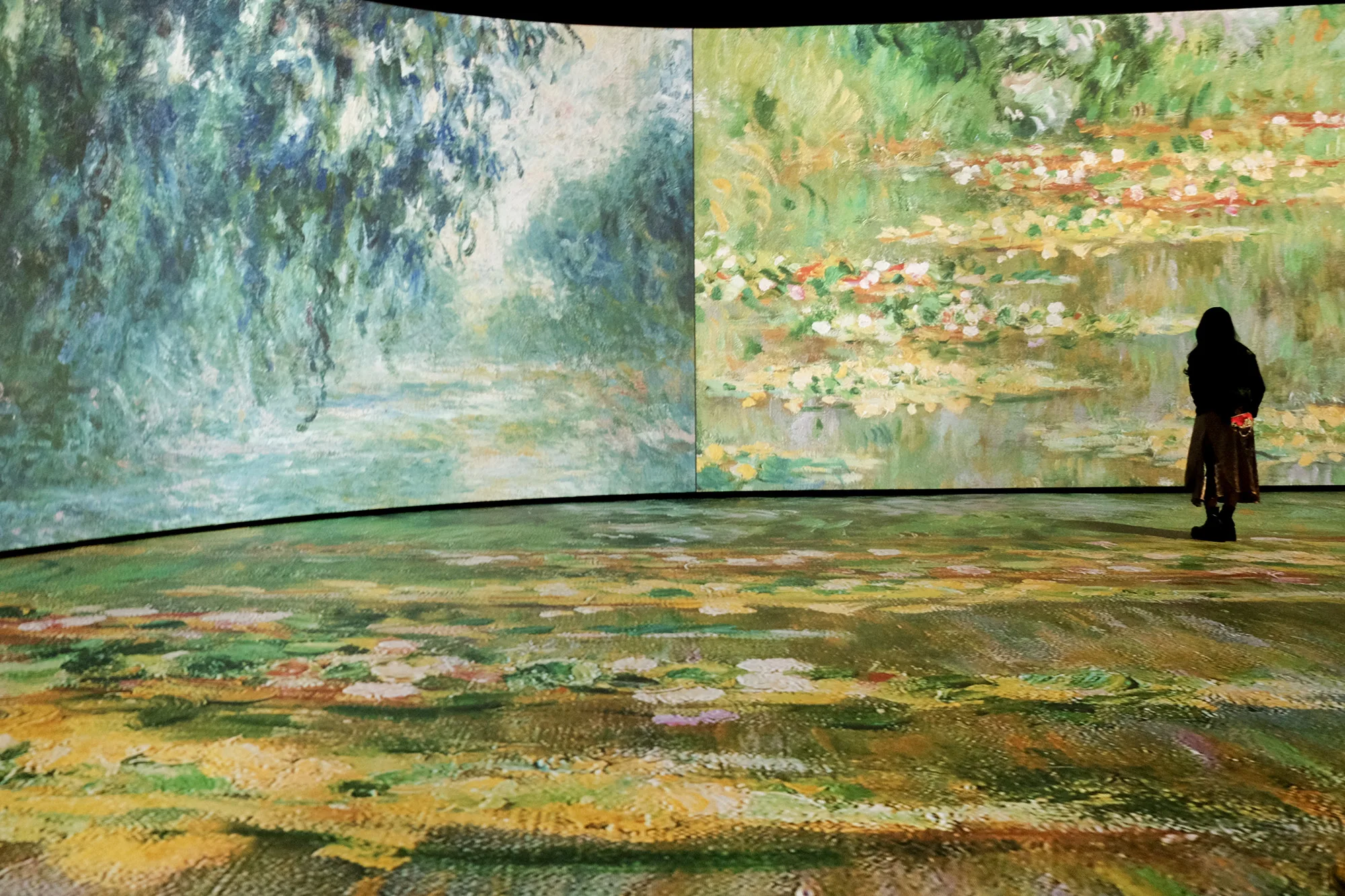 A woman stands near a wall of the Imagine Monet exhibit. The Water Lilies series is projected on the wall and floor