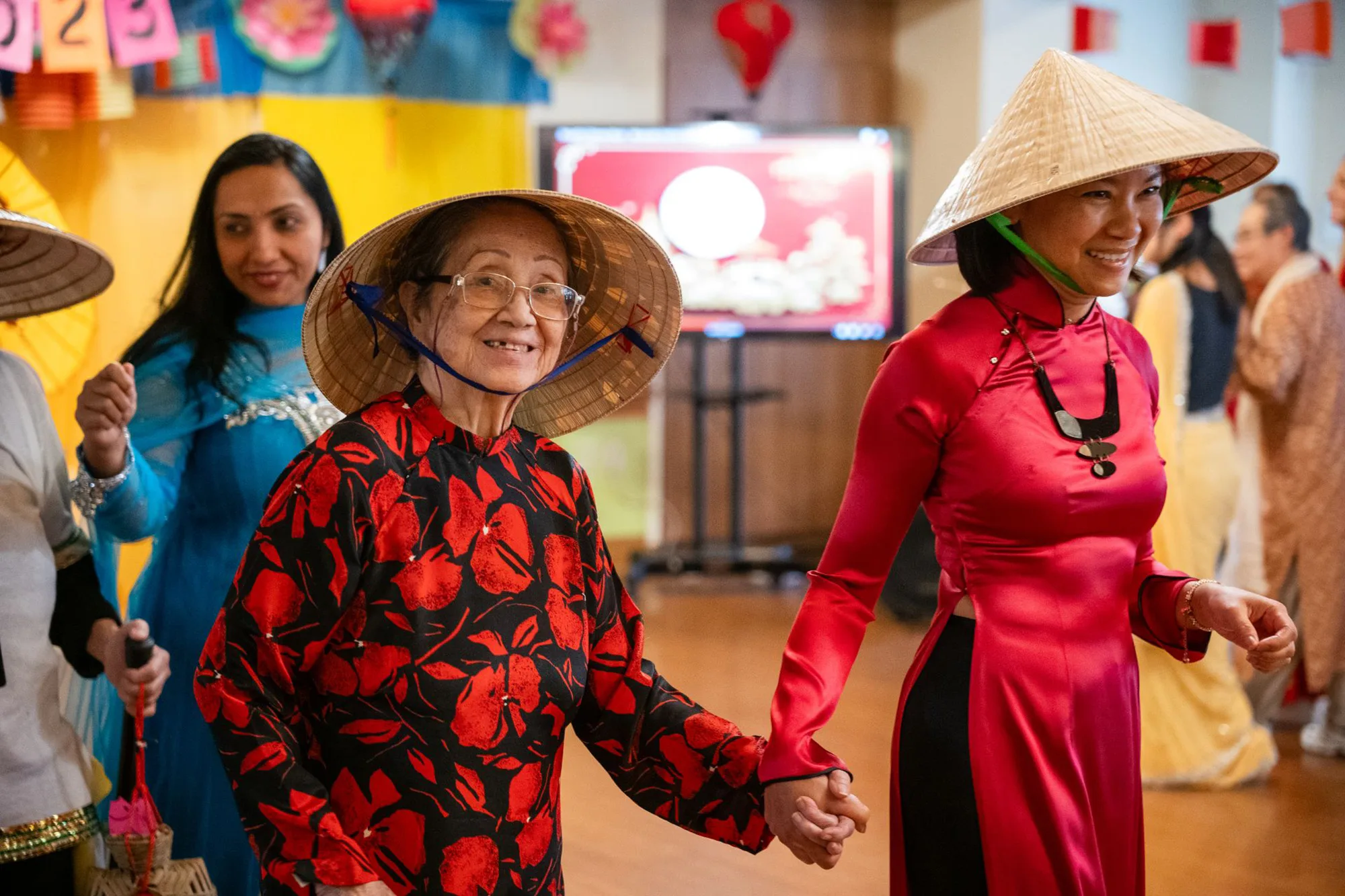 Two women, one an elder and one younger, walk side by side, smiling inside a community center