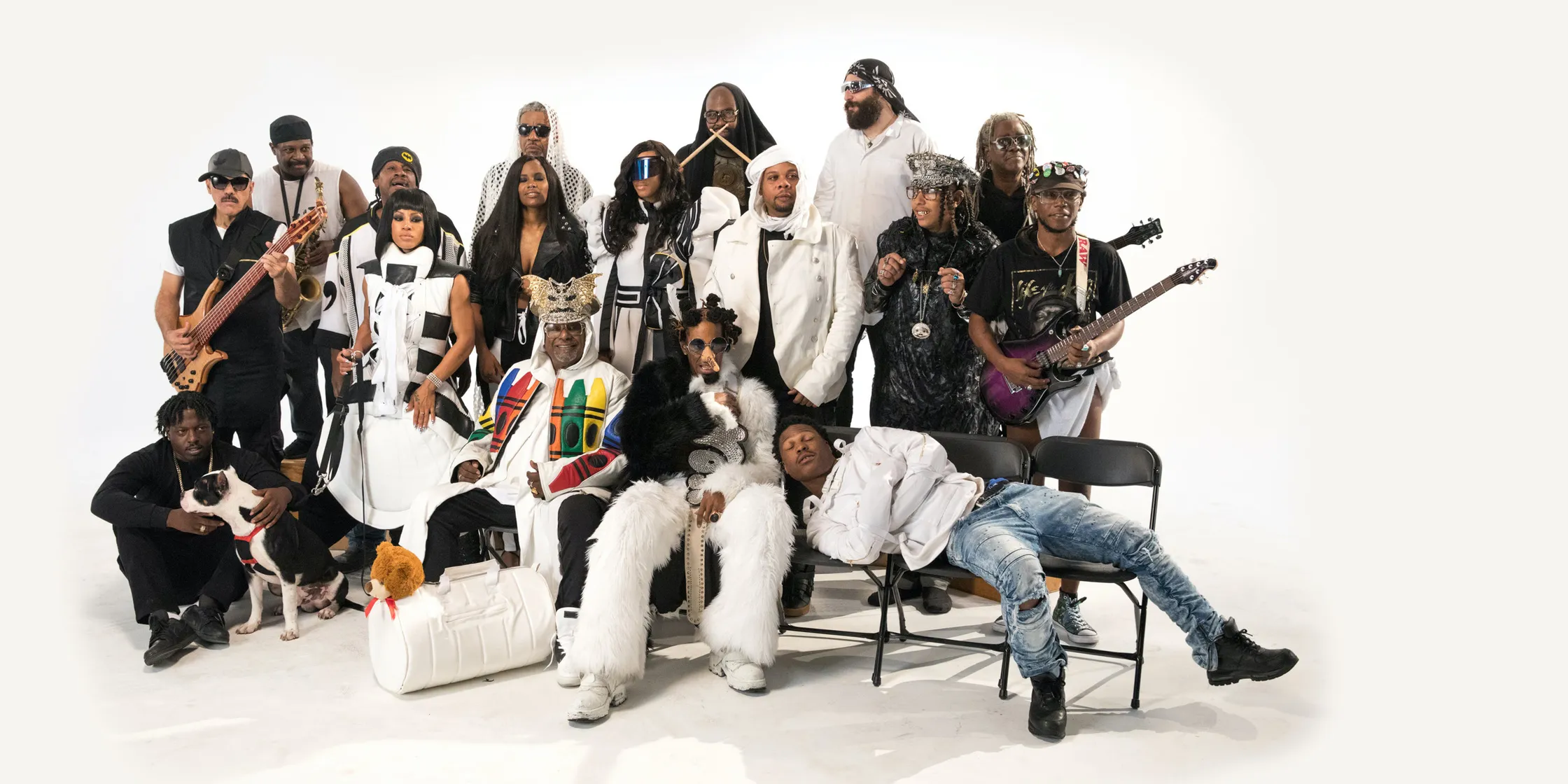 A group of musicians sit in a big white studio. Parliament Funkadelic feat. George Clinton.