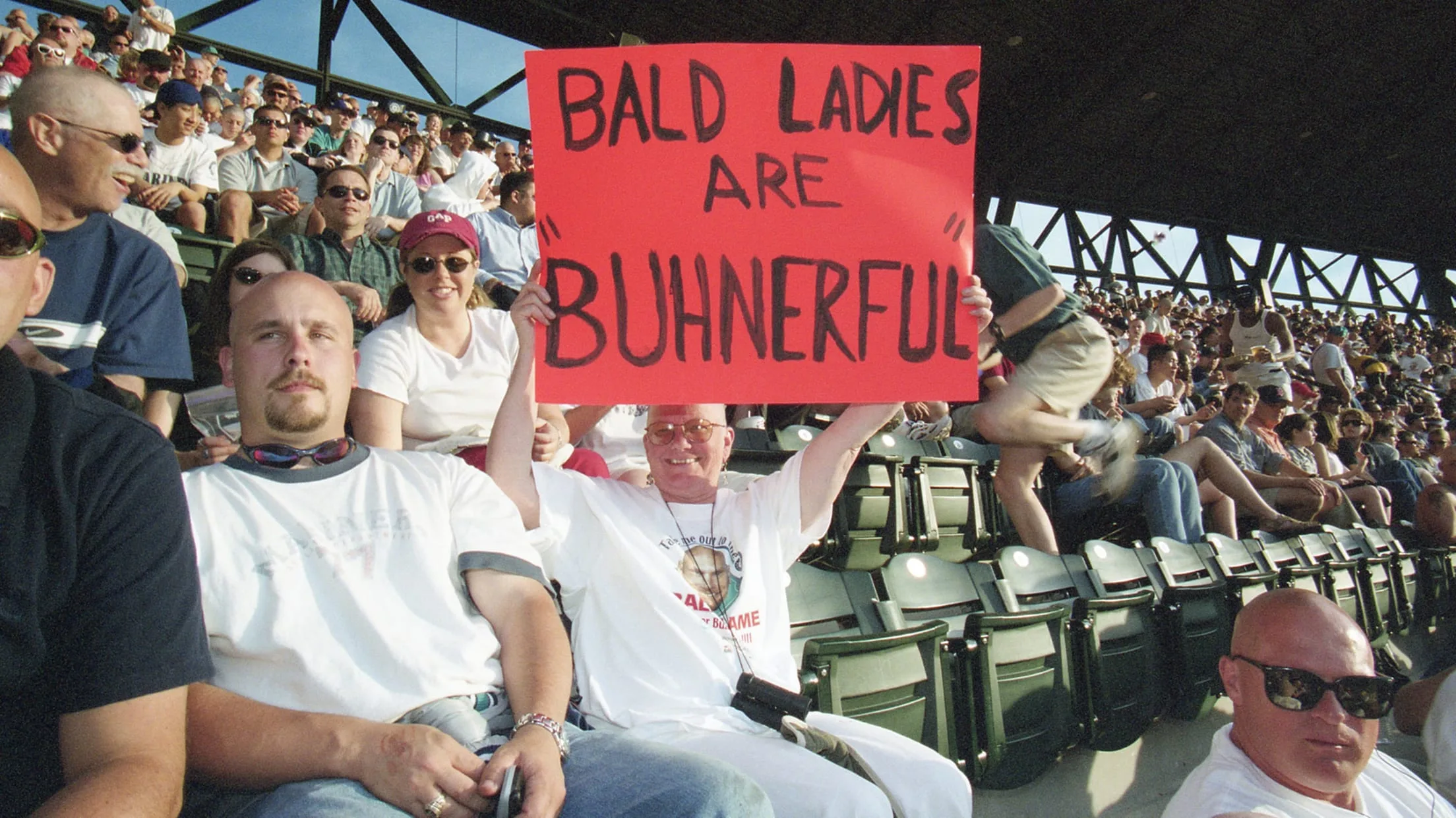 A bald woman holds up a sign that reads "BALD LADIES ARE BUHNERFUL."