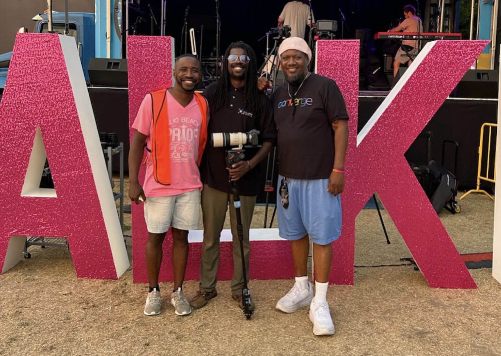 A group of three people stand in front of big letters that read "ALKI" during Alki Beach Pride.