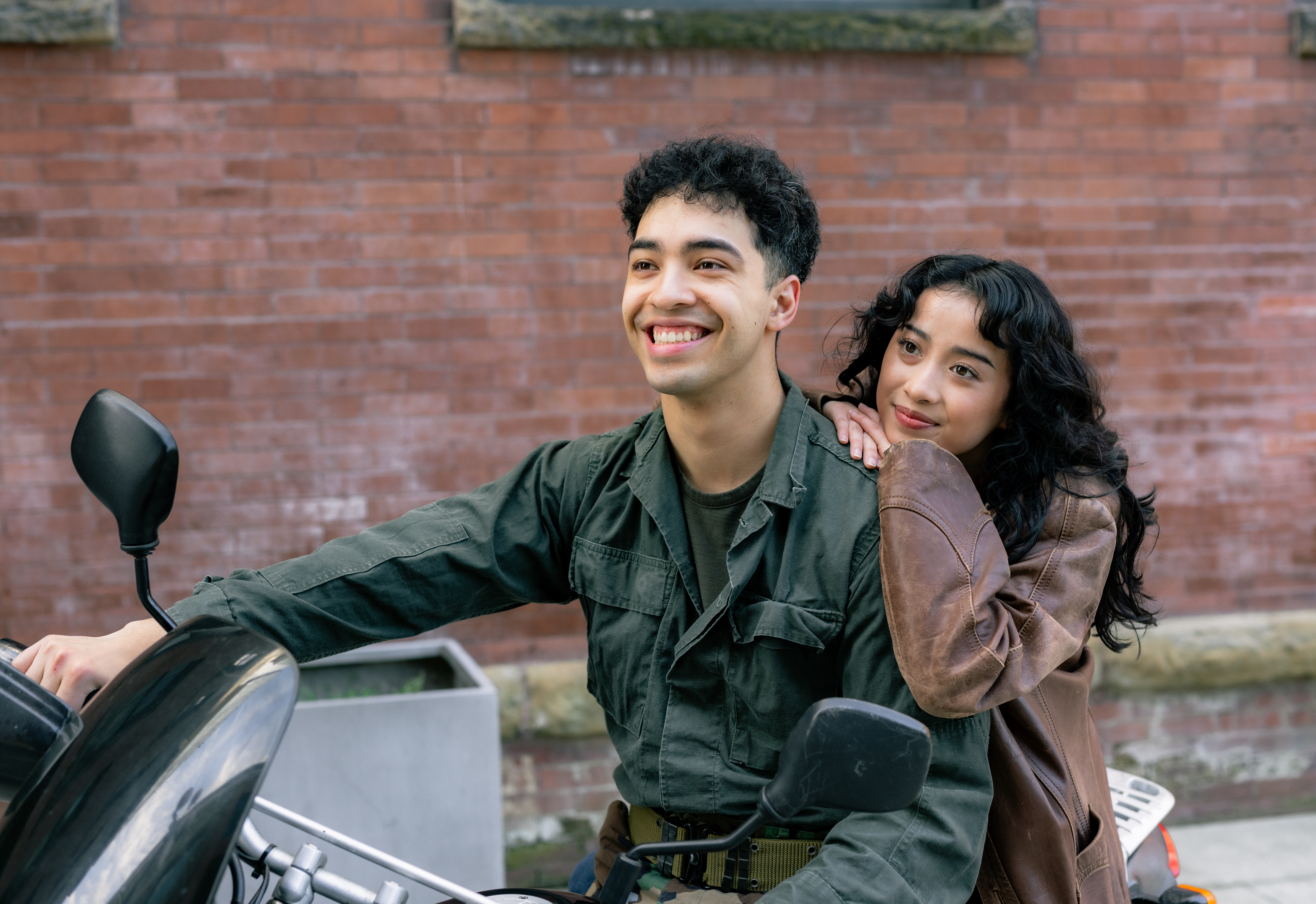 Quang (Josh Erme) and Tong (Megan Huynh). Photo by Giao Nguyen. Two people ride on a motorcycle, one of them looking lovingly while resting on the driver's shoulder.