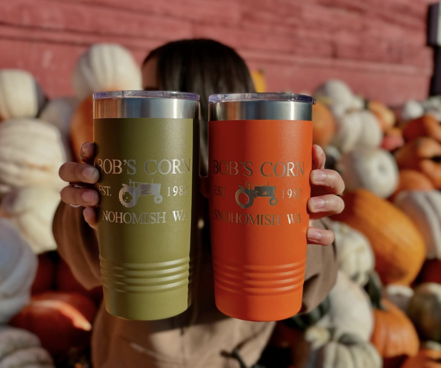 A woman holds up two mugs from Bob's Corn Maze and Pumpkin Patch.