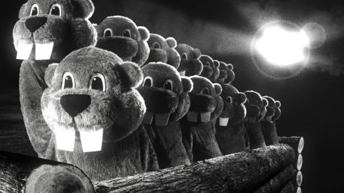 A black and white still from 'Hundreds of Beavers' showing a line of puppet beaver heads with cartoonish eyes and prominent teeth, arranged in a diminishing perspective against a moonlit sky