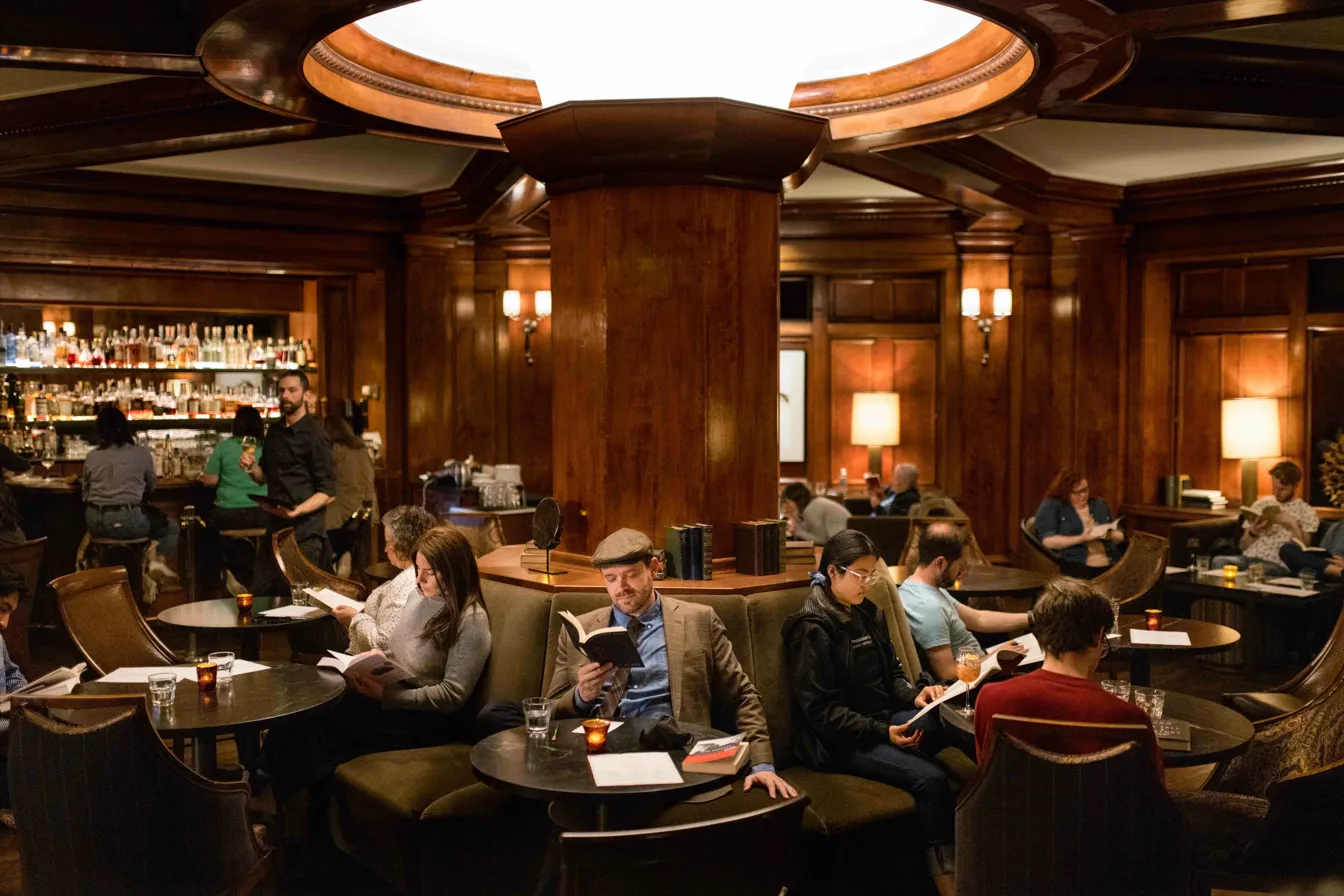 Inside the Sorrento Hotel's wood-paneled Fireside Room, readers sit in leather chairs around small tables with glowing candles. A domed skylight illuminates the warm space, while a well-stocked bar glows in the background.