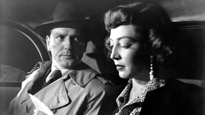 A dramatic black and white film still from The Narrow Margin (1952) featuring a tense close-up of two characters in a shadowy train compartment, highlighting film noir's characteristic use of shadow and intimate framing.