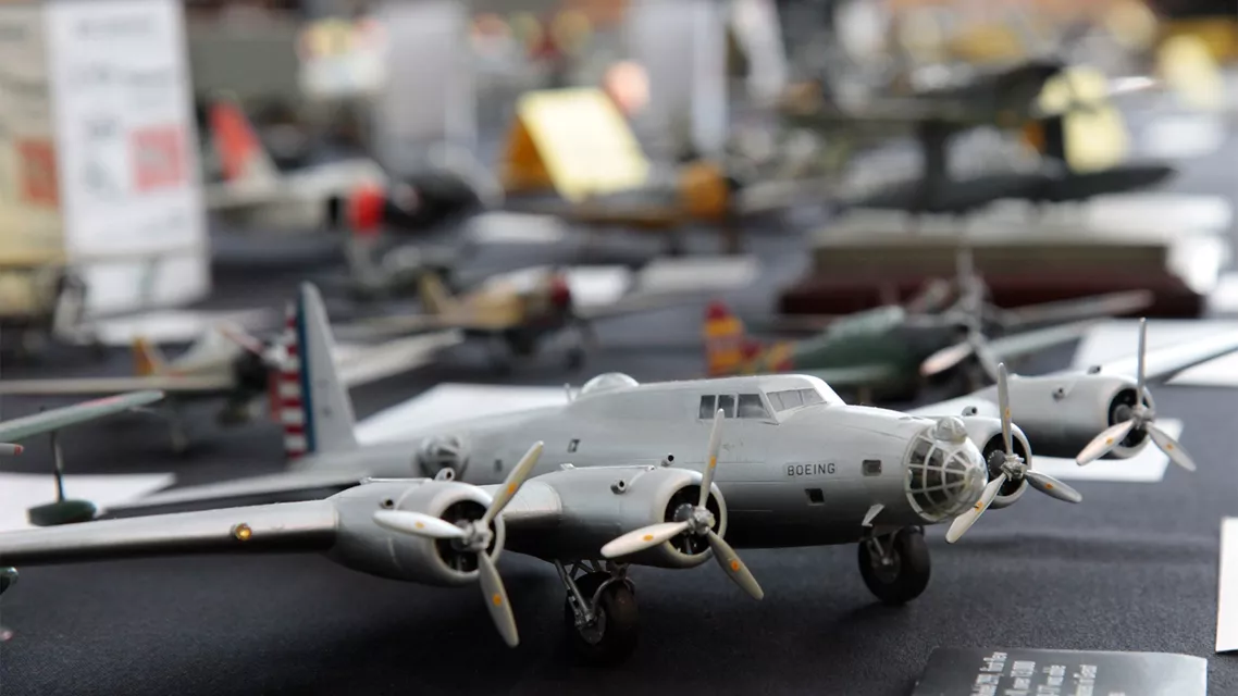 A detailed scale model of a silver Boeing B-29 Superfortress bomber sits in sharp focus on a black display table, with other miniature aircraft visible in the background.