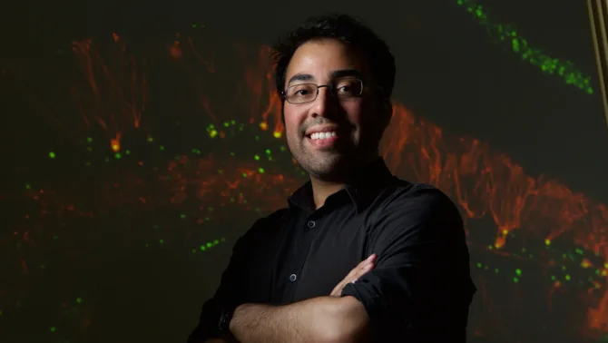 Neuroscientist Steve Ramirez stands in front of a dark background. He smiles at the camera with his arms crossed.