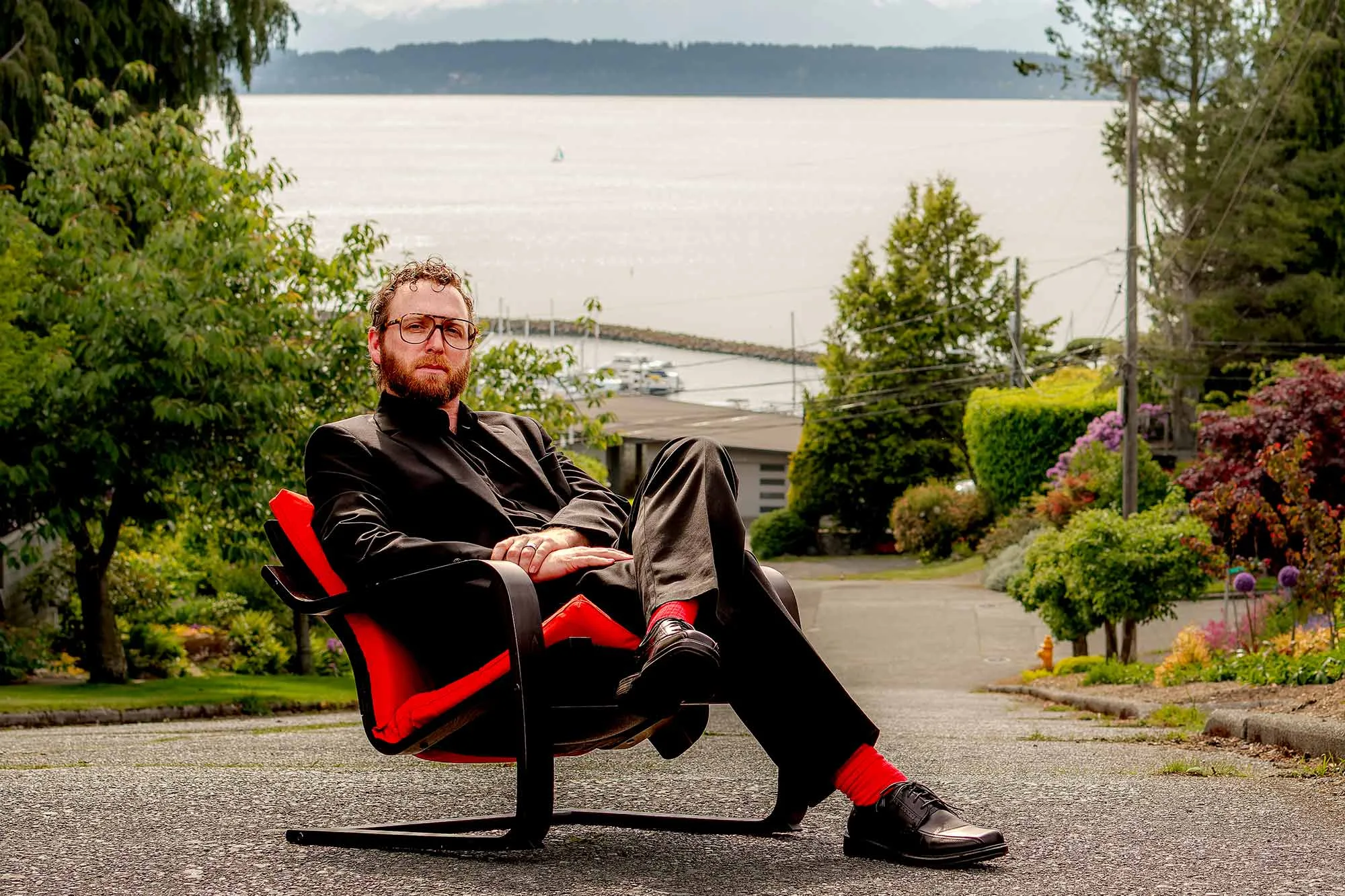 Brian Pucheu, as Ingvar Kamprad, sits in his IKEA chair in front of mountains.