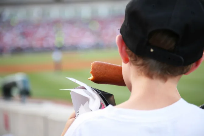 Child eating a corndog at a baseball stadium